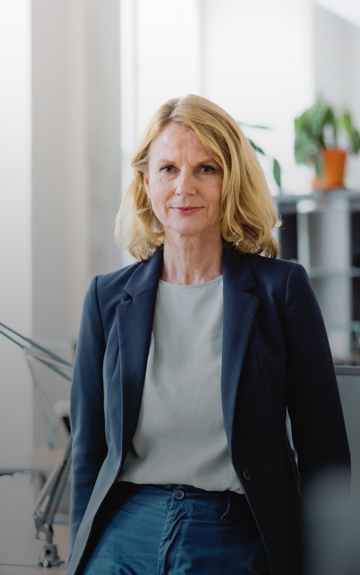 Eine Unternehmerin steht in ihrem Büro. Sie blickt direkt in die Kamera.